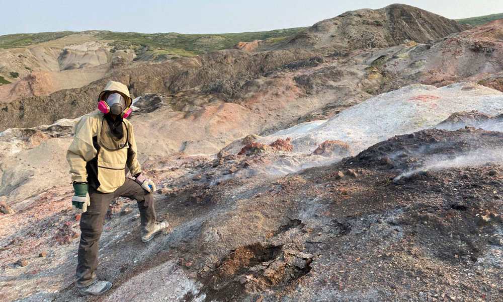 Scientist standing on a rocky hillside wearing a respirator mask.