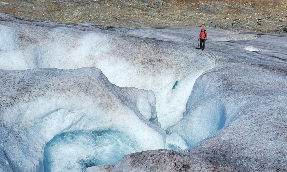A scientist stands on the edge of a massive hole in a glacier.