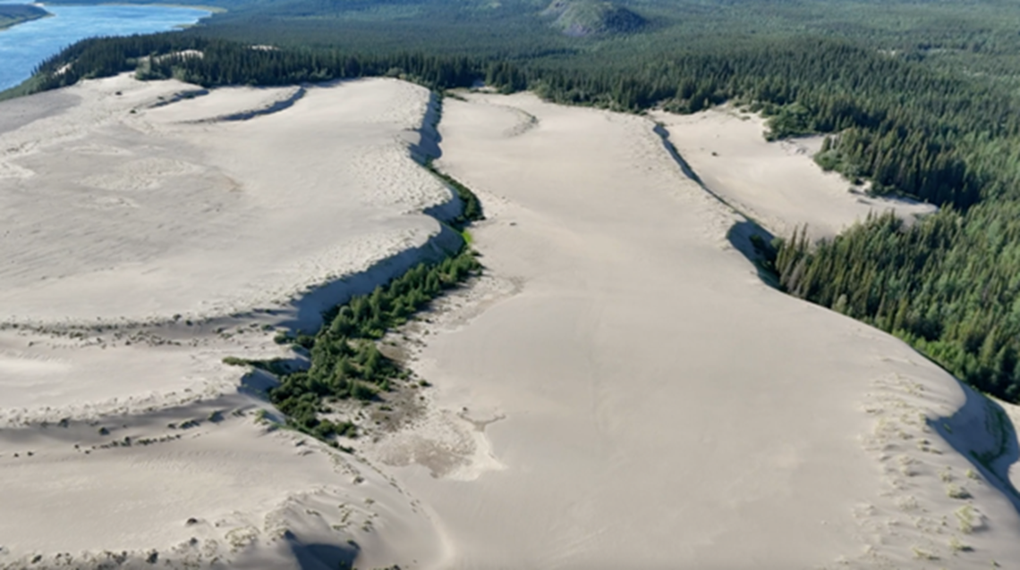 Wide aerial image of large sand dunes bordered by evergreen trees. Map of region (Geo.ca).
