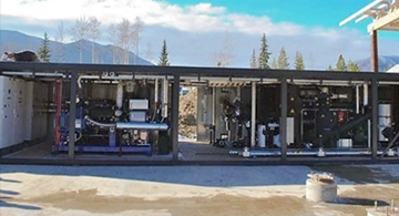 Outdoor view of a modular geothermal power generation unit housed in a large open steel container.