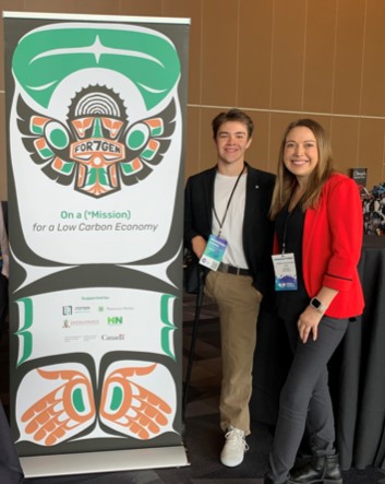 Two people wearing lanyards stand next to a sign that says, “On a (*Mission) for Low Carbon Economy.”