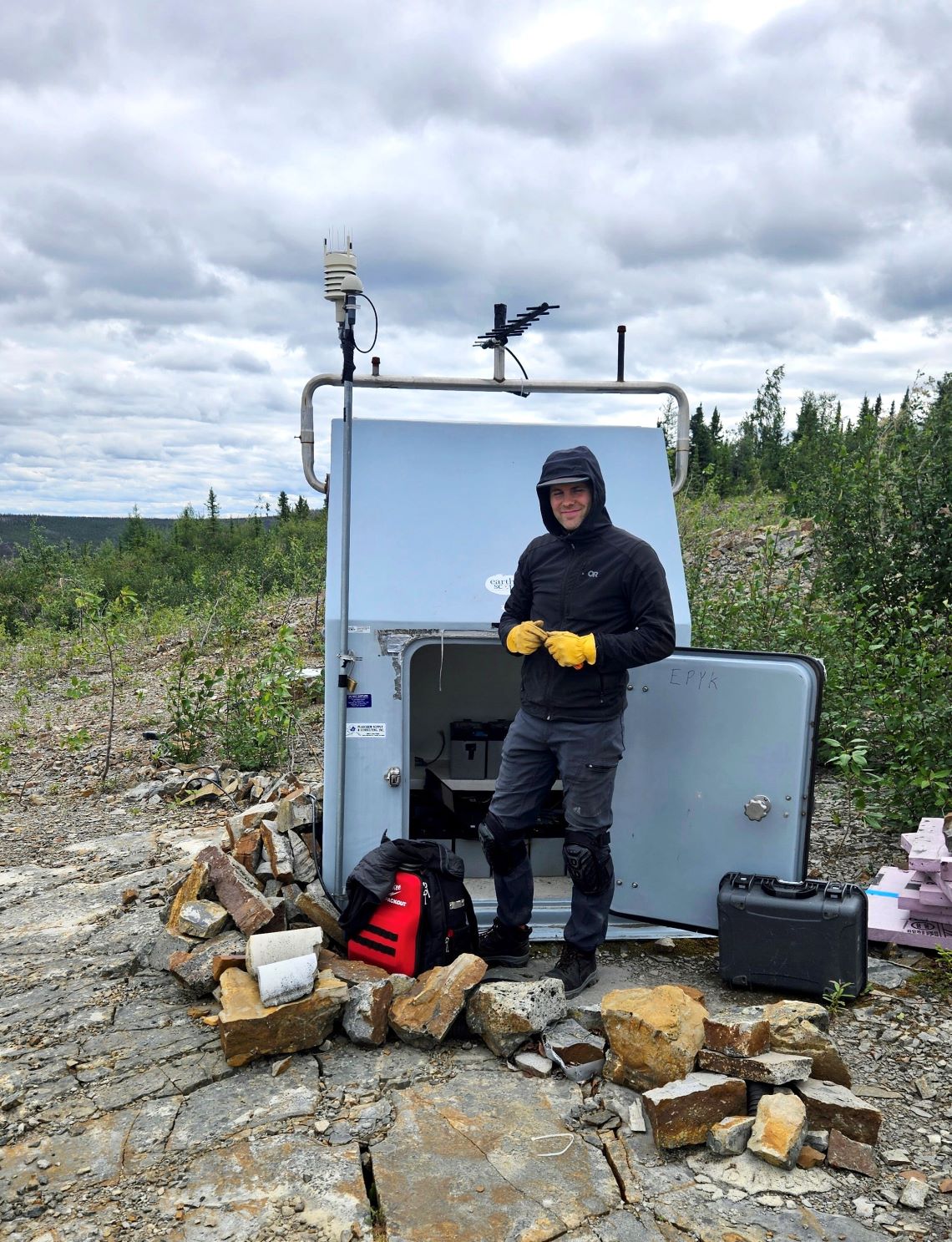 Scientist standing in front of an NRCan seismic station in the Yukon wilderness.