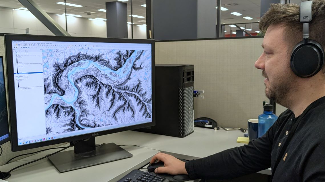A man sits in front of a computer. The screen displays a river with elevation data. 