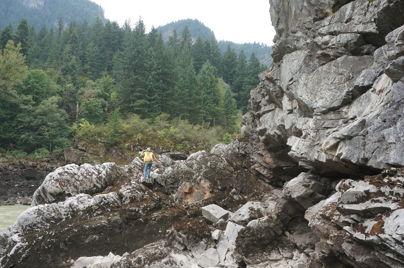 A surveyor working among exposed rock formations and forested terrain.