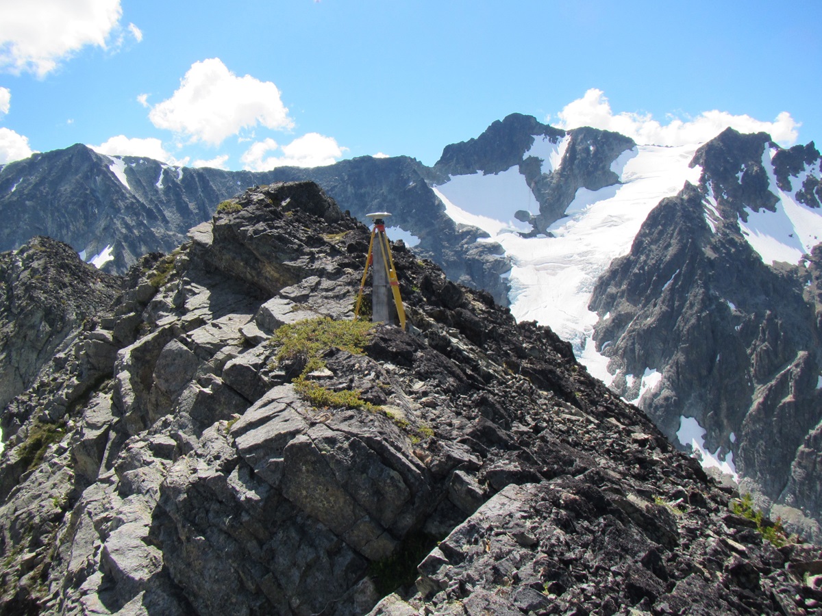 A mountainous boundary landscape illustrating IBC field operations, with a survey marker and tripod positioned on exposed alpine rock.