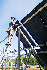 A worker on a ladder installing a solar panel on a sunny day.