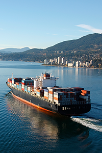A cargo ship sailing on the ocean with a city in the background.