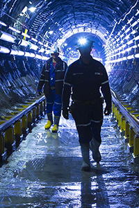 Two Cameco workers in hard hats walk through an underground tunnel.