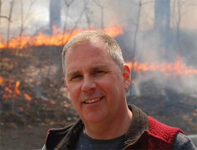 Mike Wotton with a forest fire burning behind him.